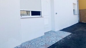 A white building with a garage door, a small window, and a tiled entrance.