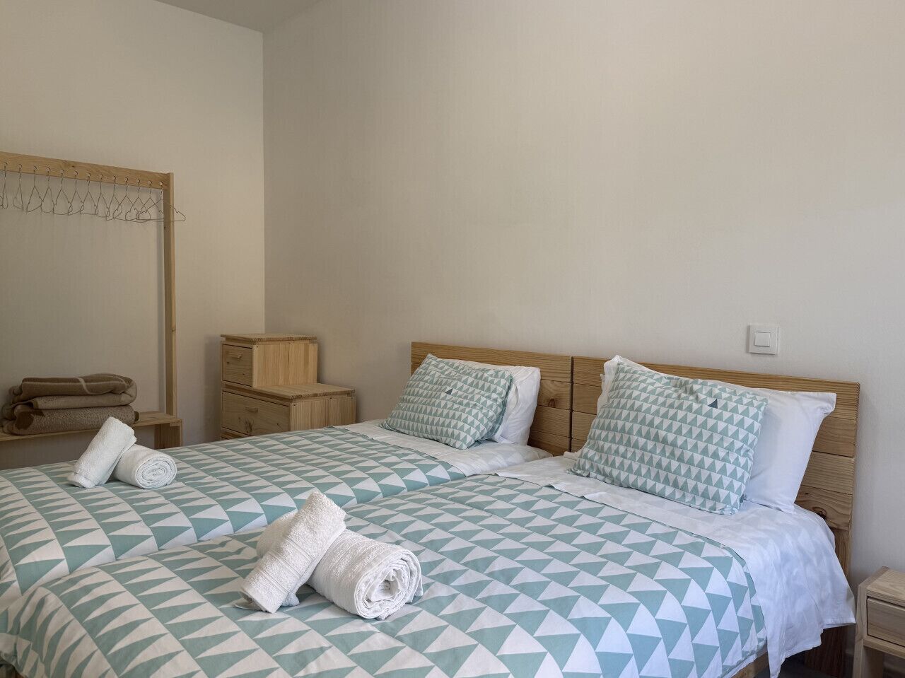 A double bed with a geometric patterned bedspread, two pillows, a wooden nightstand, a wooden dresser, and a mirror on the wall.