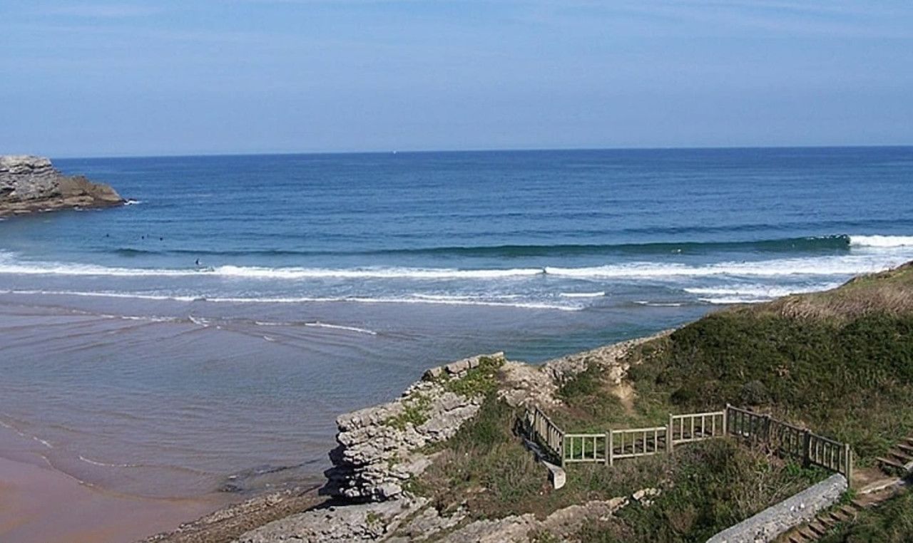 Vista costera con costa rocosa, una pasarela de madera y el océano al fondo.
