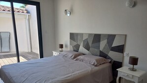 Ein Schlafzimmer mit einem Bett, zwei Nachttischen, einem Kopfteil mit geometrischem Muster und einer Schiebetür zu einem Außenbereich.