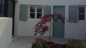 Ein Innenhof mit einem Blumentopf, einem kleinen Blumenbeet und einem Gebäude mit weißen Wänden und grünen Fensterläden.