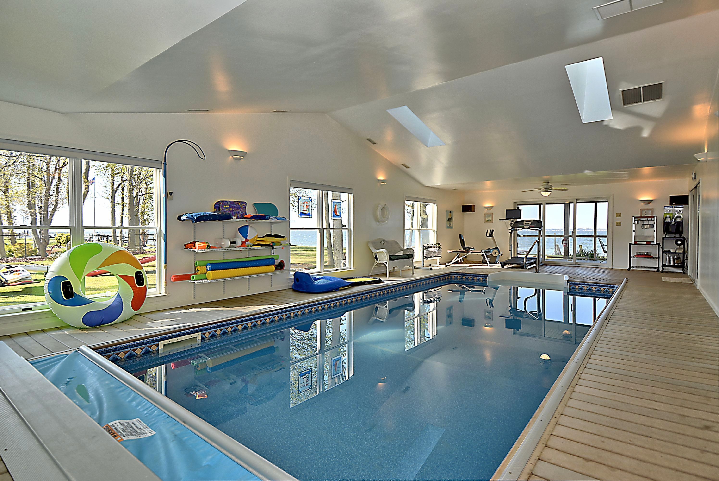 Une grande piscine intérieure avec de larges baies vitrées, un ventilateur de plafond et du matériel d’exercice.