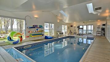 Une grande piscine intérieure avec de larges baies vitrées, un ventilateur de plafond et du matériel d’exercice.