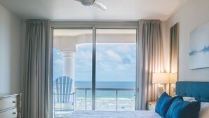 Ein Hotelzimmer mit einem großen Bett, einem Deckenventilator, Meerblick und einem Balkon mit einem Stuhl.