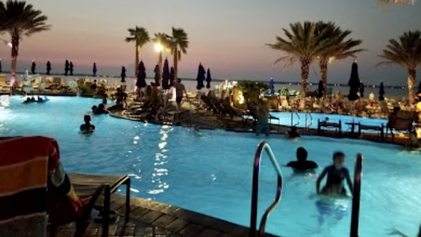 Ein Poolbereich mit Palmen und Liegestühlen, umgeben von einer Poolterrasse.
