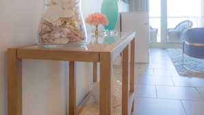 Ein Hotelzimmer mit einem Holztischchen, einer Glasvase mit Blumen, einer türkisblauen Lampe, einem Spiegel und Blick auf den Balkon.