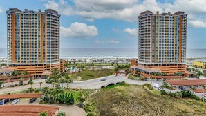 Ein Hochhaus-Hotel mit mehreren Balkonen, Blick auf den Strand und einem Parkbereich mit überdachten Parkhäusern.