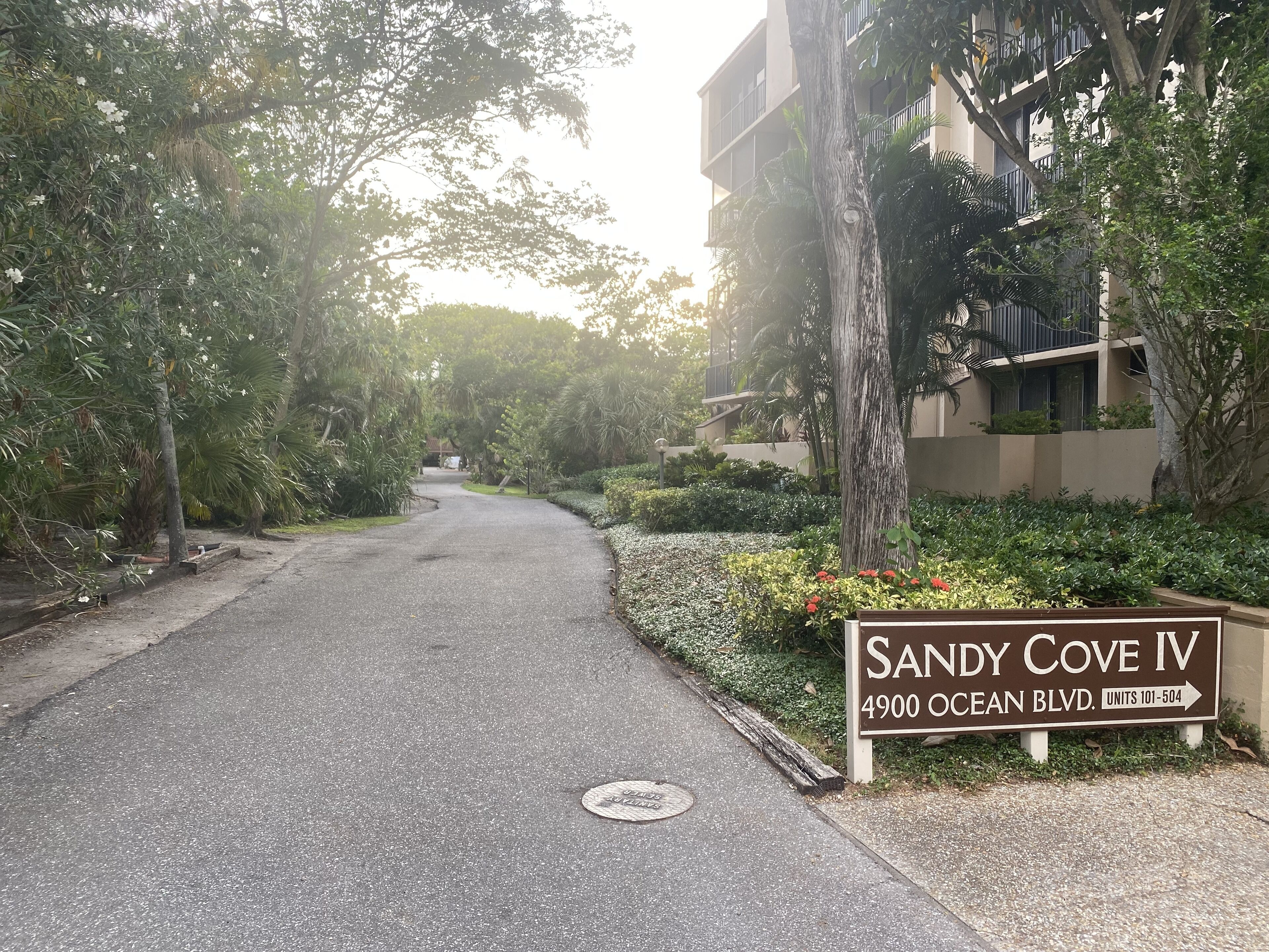 Naamplaatje voor Sandy Cove IV op Ocean Boulevard 4900, met een pad dat naar een gebouw leidt.