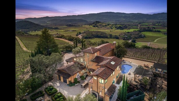 Una villa con varias construcciones, piscina y campos de viñedos al fondo.