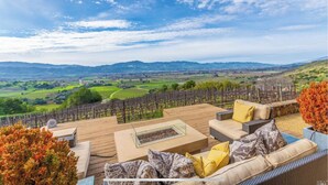 Una terraza con mobiliario exterior, una chimenea y vistas a un viñedo.
