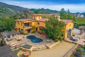 Relax in a spacious courtyard with a swimming pool surrounded by outdoor seating areas, offering scenic views of the hilly landscape.
