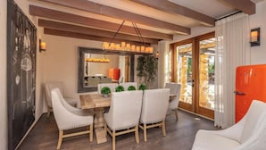 Un comedor con una mesa de madera y sillas blancas tapizadas, un espejo sobre la mesa y un refrigerador rojo al fondo.