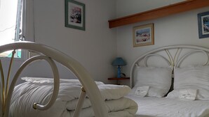 Una cama bien hecha con sábanas blancas, una lámpara de noche y cuadros en la pared.