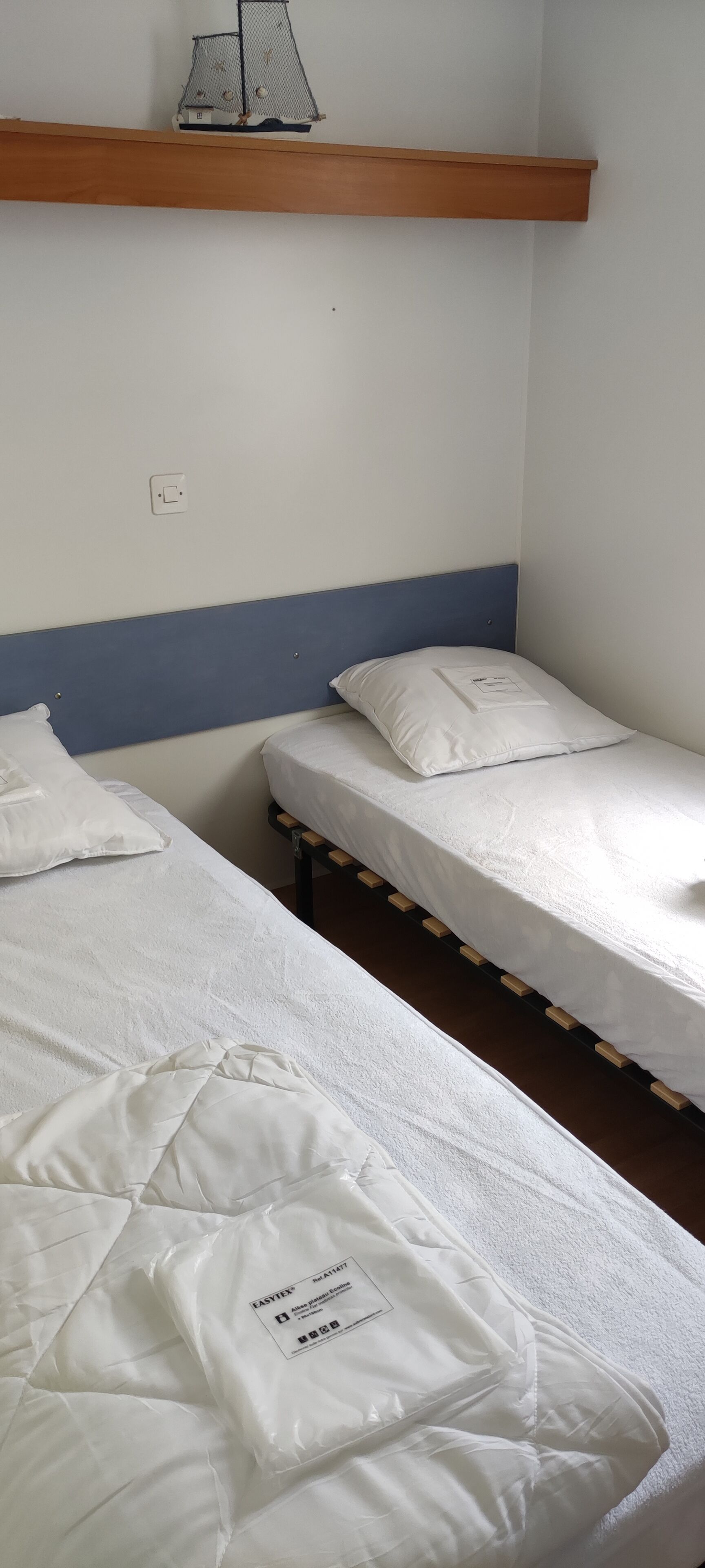 Ein Zimmer mit zwei Einzelbetten, einem Holzregal darüber und einer Steckdose.