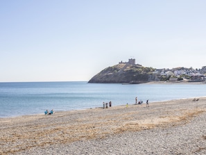 A pebble beach with a castle on a hill, calm sea, and people relaxing.