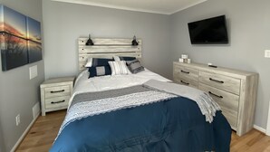 A bedroom with a bed, nightstands, a dresser, a ceiling fan, a TV, and artwork on the wall.