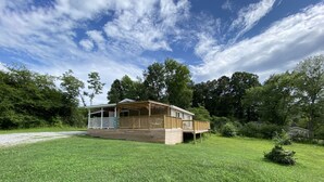 A wooden cabin with a porch and deck, surrounded by lush greenery and trees.
