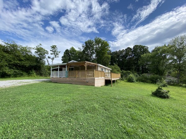 A wooden cabin with a porch and deck, surrounded by lush greenery and trees. - Harrison Bay Hideaway: Cozy home, walk to Harrison Bay State Park, Golf, Lake (Harrison)