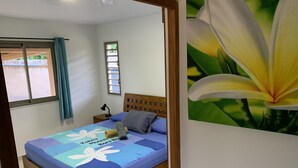 Un dormitorio con una cama, una mesita de noche, un ventanal con cortinas y una pared decorada con una pintura de flores.