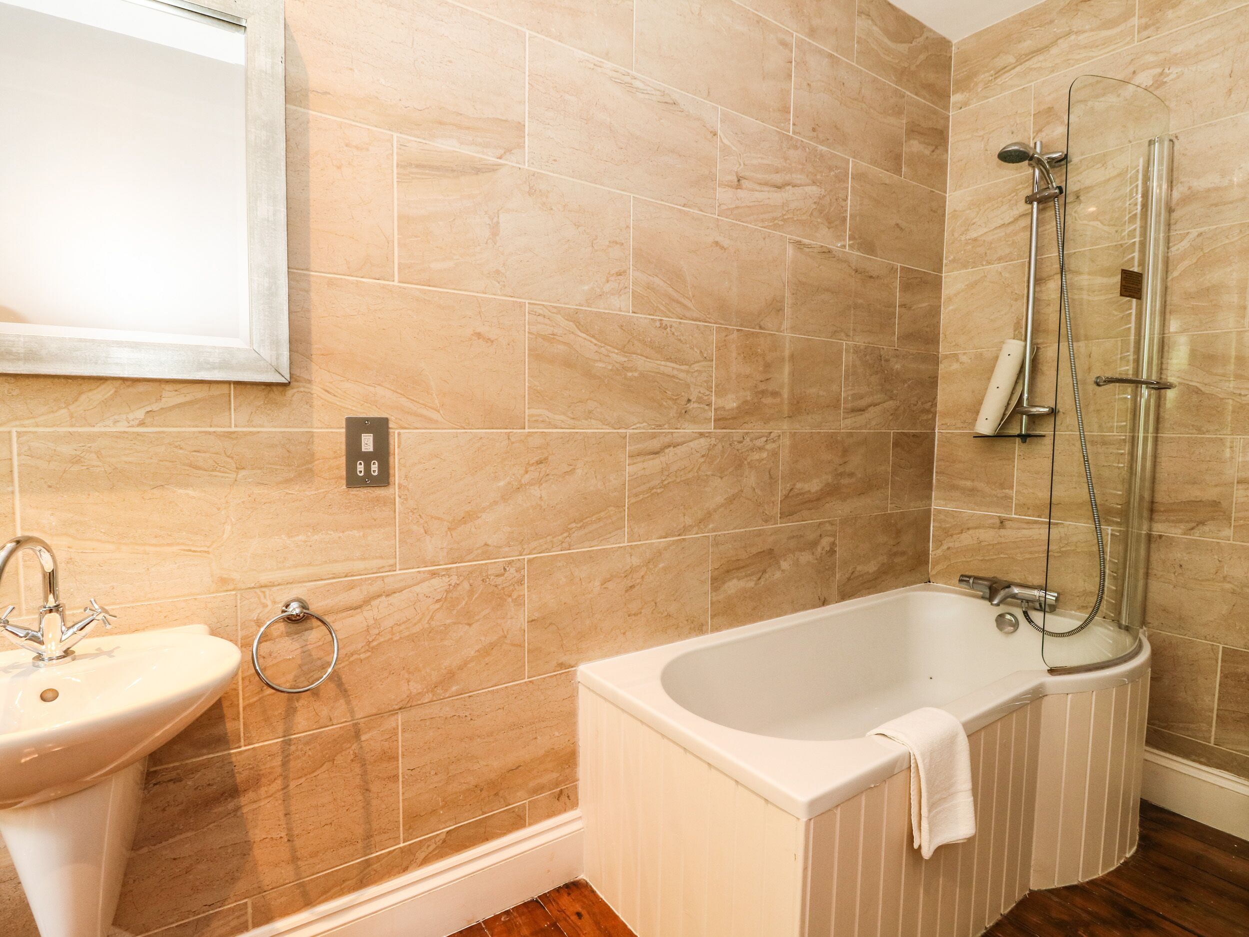 A bathroom with beige marble tiles, a white sink, and a bathtub with a towel.