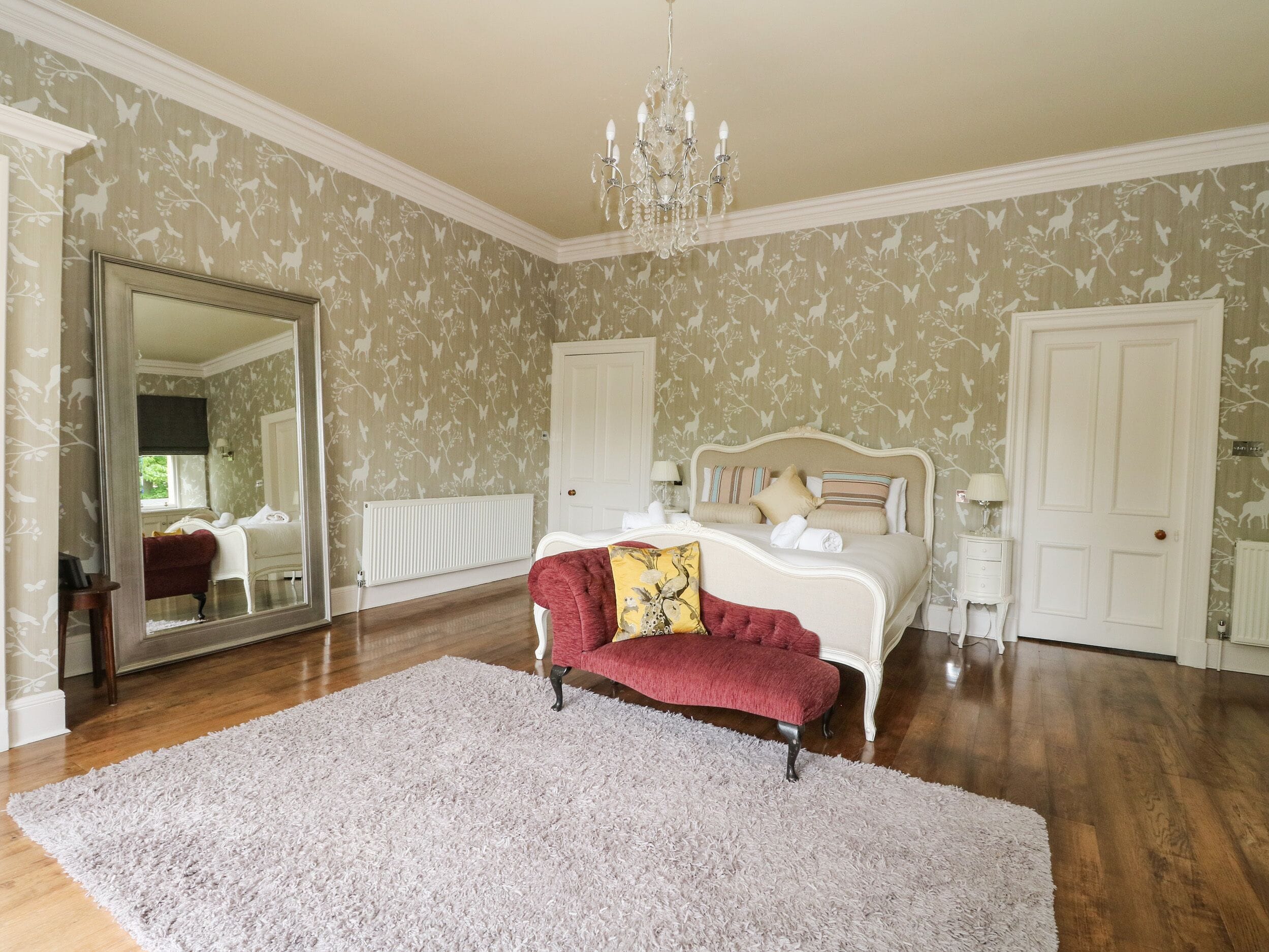Een slaapkamer met een grote spiegel, een bed met veel kussens, een rode bank en een kroonluchter.