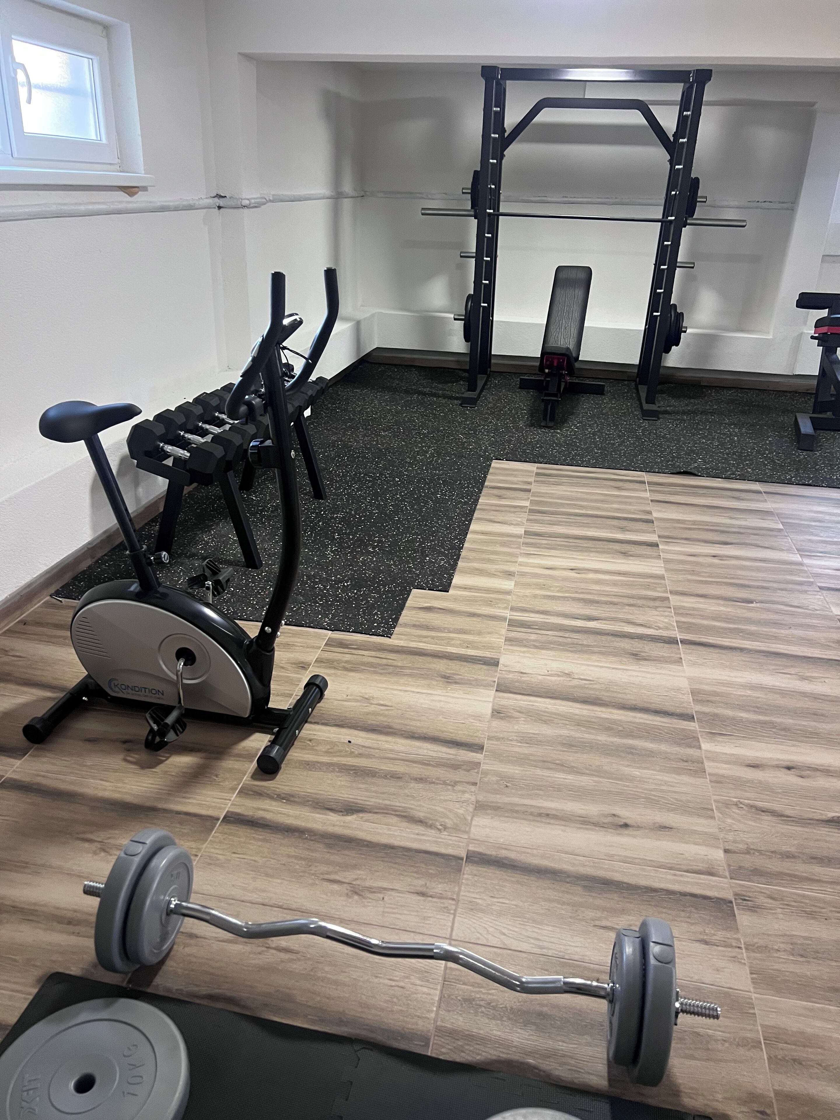 A home gym with a stationary bike, a bench press, and a barbell.