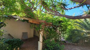 A covered outdoor area with a pergola, a wall-mounted easel, and lush greenery. - Very nice, quiet apartment near the beach (Hyères)