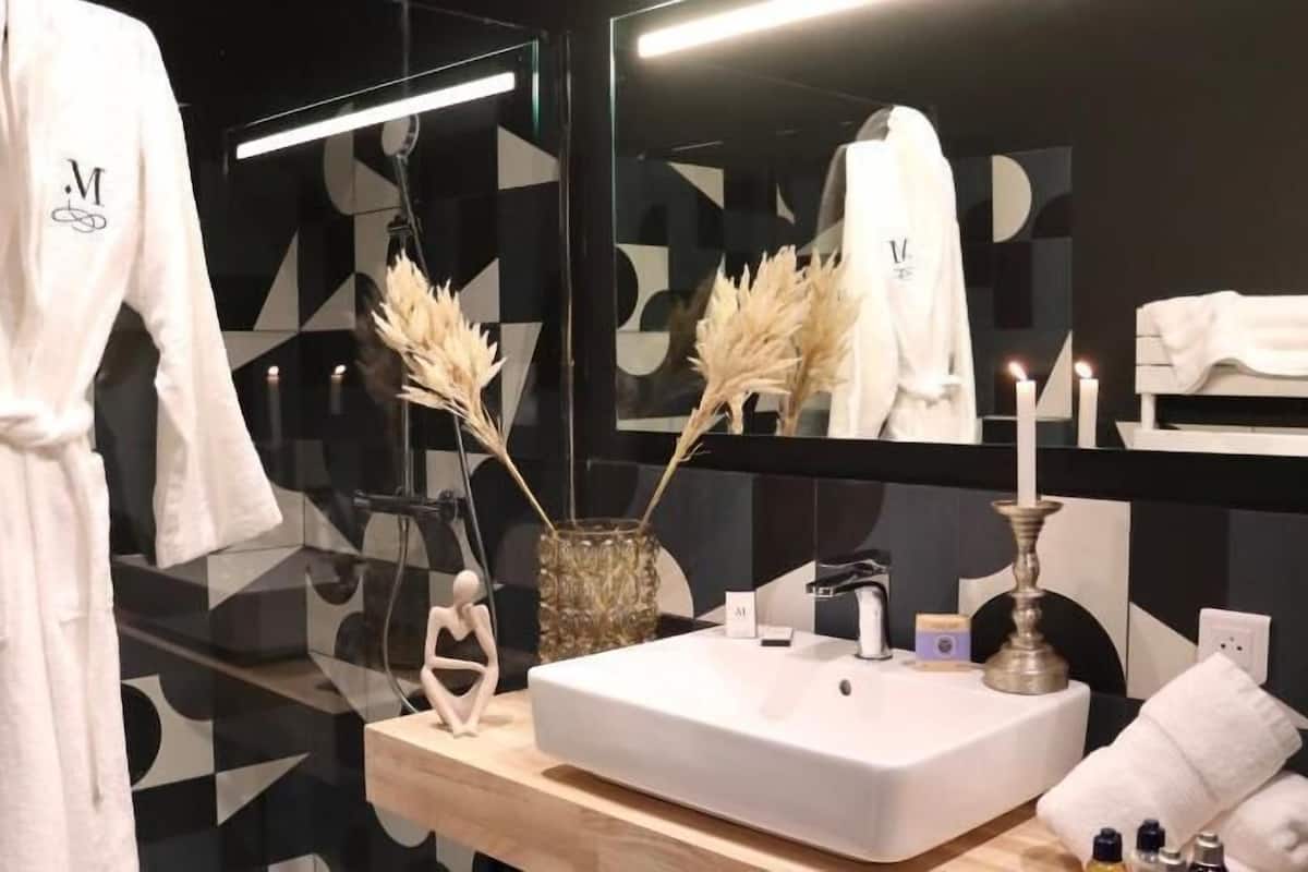 A modern bathroom with a white sink, mirror, and a robe hanging on the wall.
