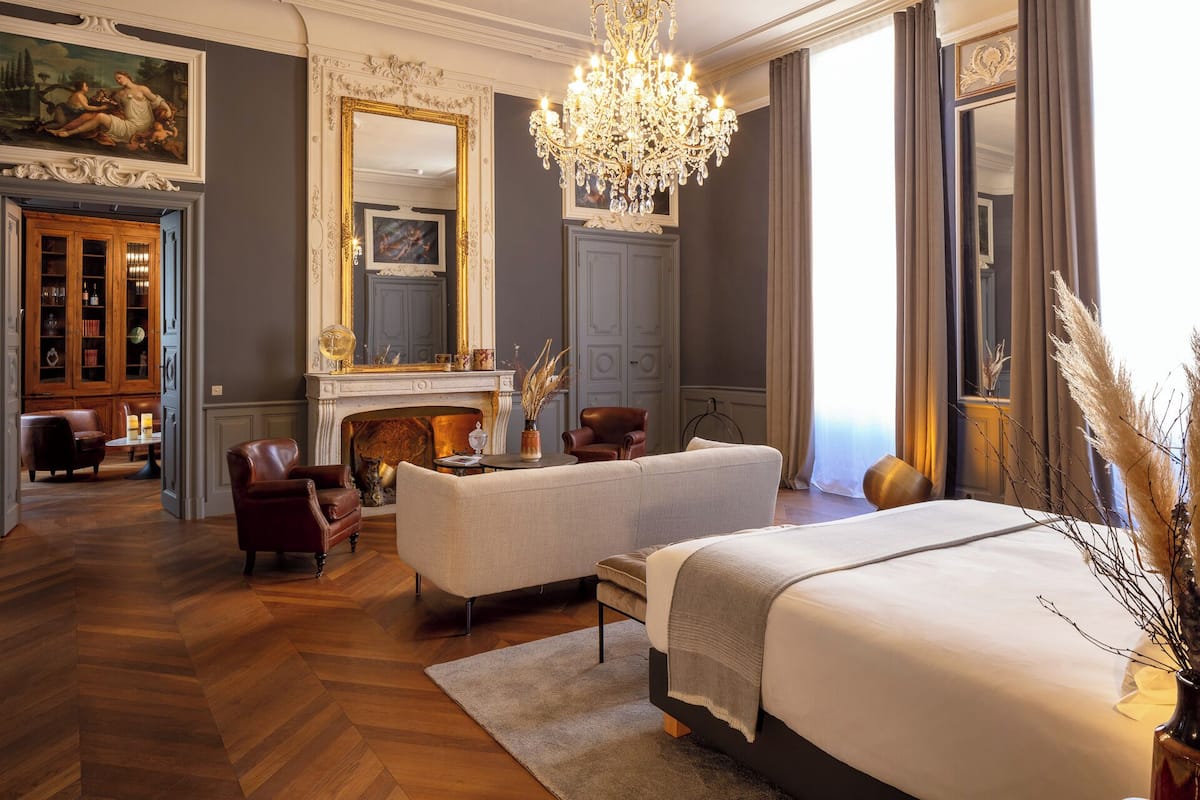 A luxurious bedroom with a large bed, a fireplace, a chandelier, and a classic decor style.