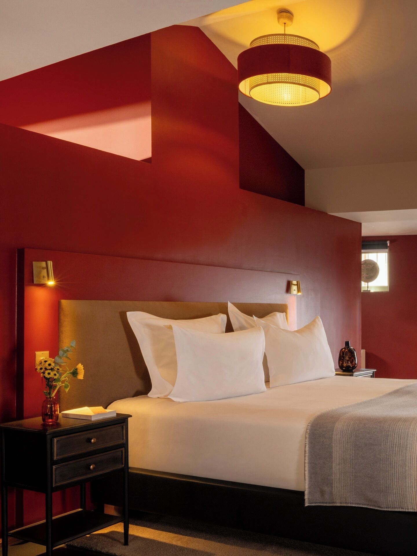 A hotel room with a large bed, a nightstand, a vase with flowers, and a ceiling light fixture.