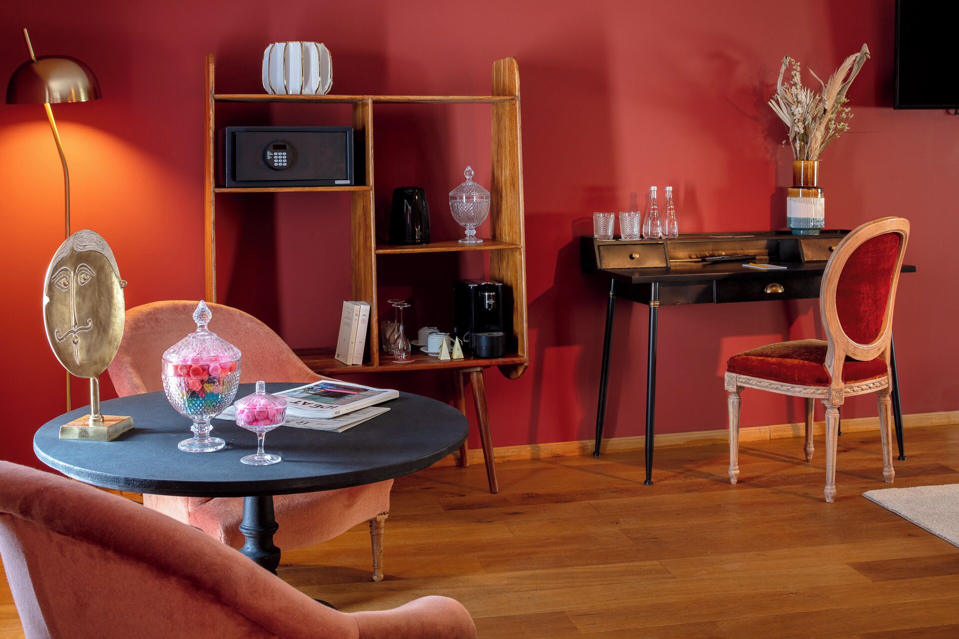 A room with a round table, a chair, a bookshelf, a desk, and a lamp.