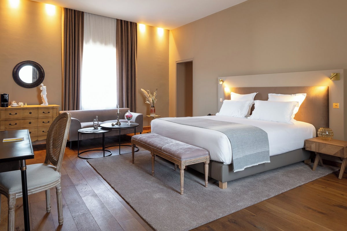 A modern hotel room with a large bed, bedside tables, a desk, and a seating area.