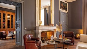 A room with a fireplace, leather armchairs, a coffee table, and a bookshelf. - Margaret - Hôtel Chouleur (Nîmes)