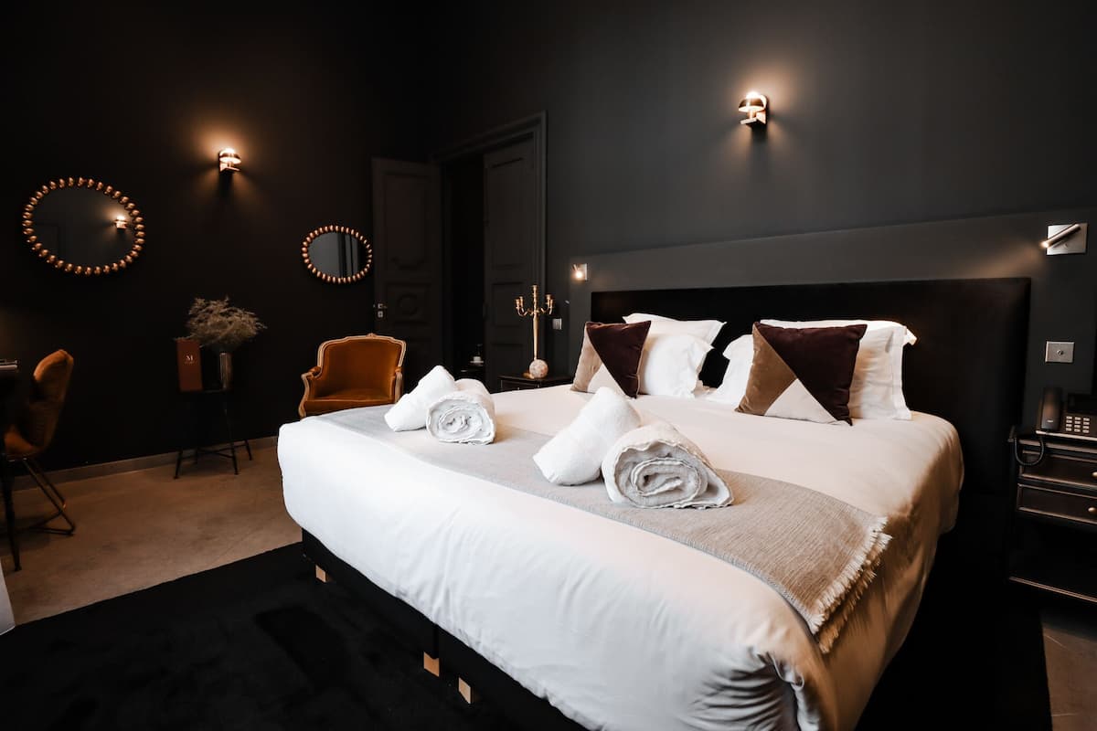 A modern hotel room with a large bed, a chair, a desk, and a mirror.