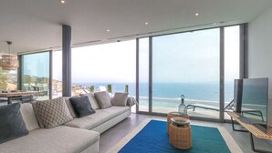 A modern living room with a large sofa, a coffee table, and a TV. The room has large windows offering a view of the ocean. - VILLA MARGARIT (Rosas / Roses)