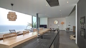 A modern kitchen with a large island, a dining area with a view of the ocean, and a cozy seating area with a large mirror and floor lamp. - VILLA MARGARIT (Rosas / Roses)