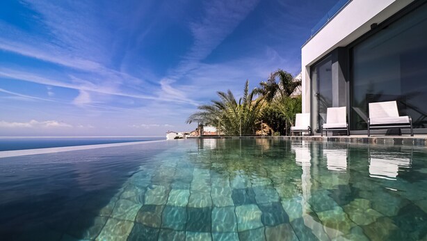 An infinity pool with clear water, a modern building with large windows, and a view of the ocean. - VILLA MARGARIT (Rosas / Roses)