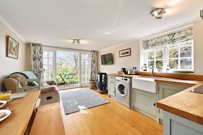 Een compacte keuken met een wasmachine, een eethoek met een tafel en stoelen, en een groot raam met gordijnen.