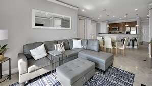 A modern living room with a grey sectional sofa, a matching ottoman, and a dining area with a table and chairs.