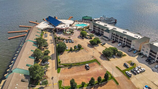 An aerial view of a waterfront hotel with a swimming pool, parking area, and docked boats.