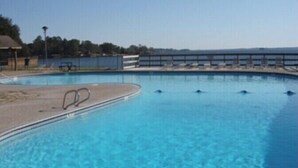 A clear blue swimming pool with a diving board, surrounded by a deck area and a view of the sea.