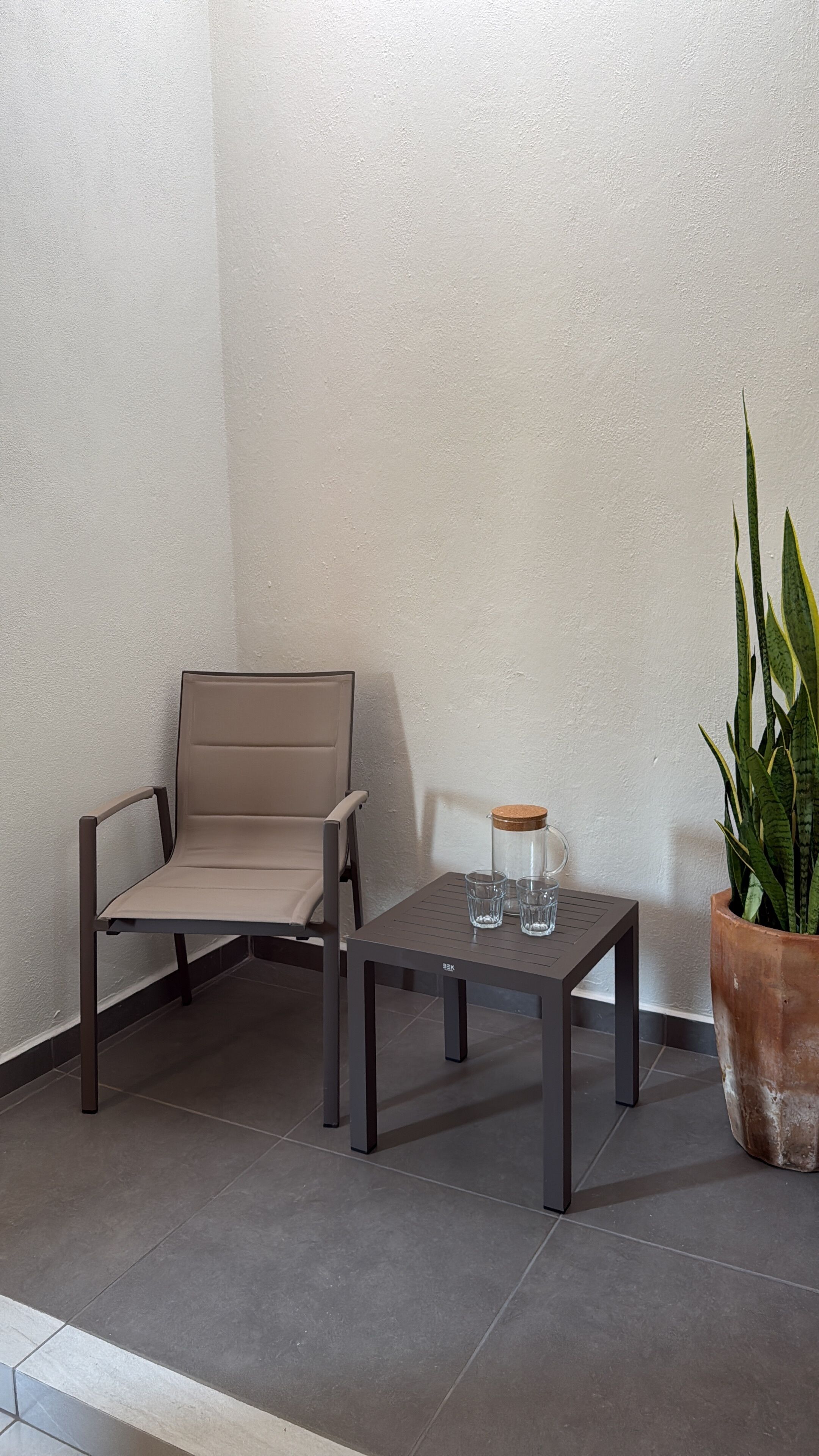 A corner seating area with a chair and a table, a potted plant, and a glass container on the table.