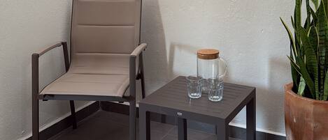 A corner seating area with a chair and a table, a potted plant, and a glass container on the table.