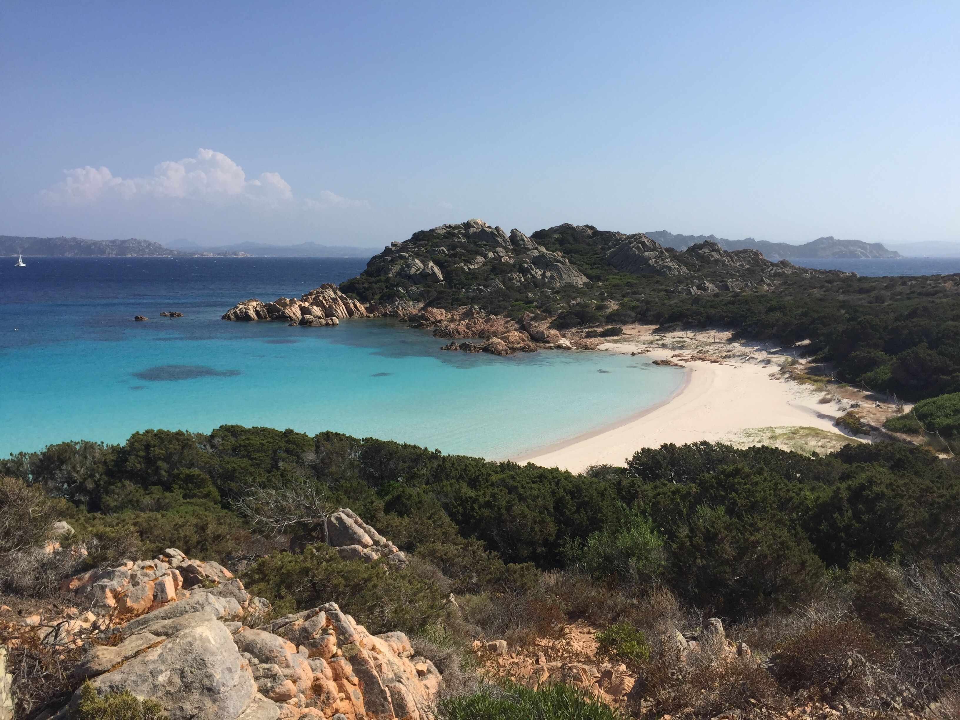 A coastal landscape with a sandy beach, rocky outcrops, and dense greenery.