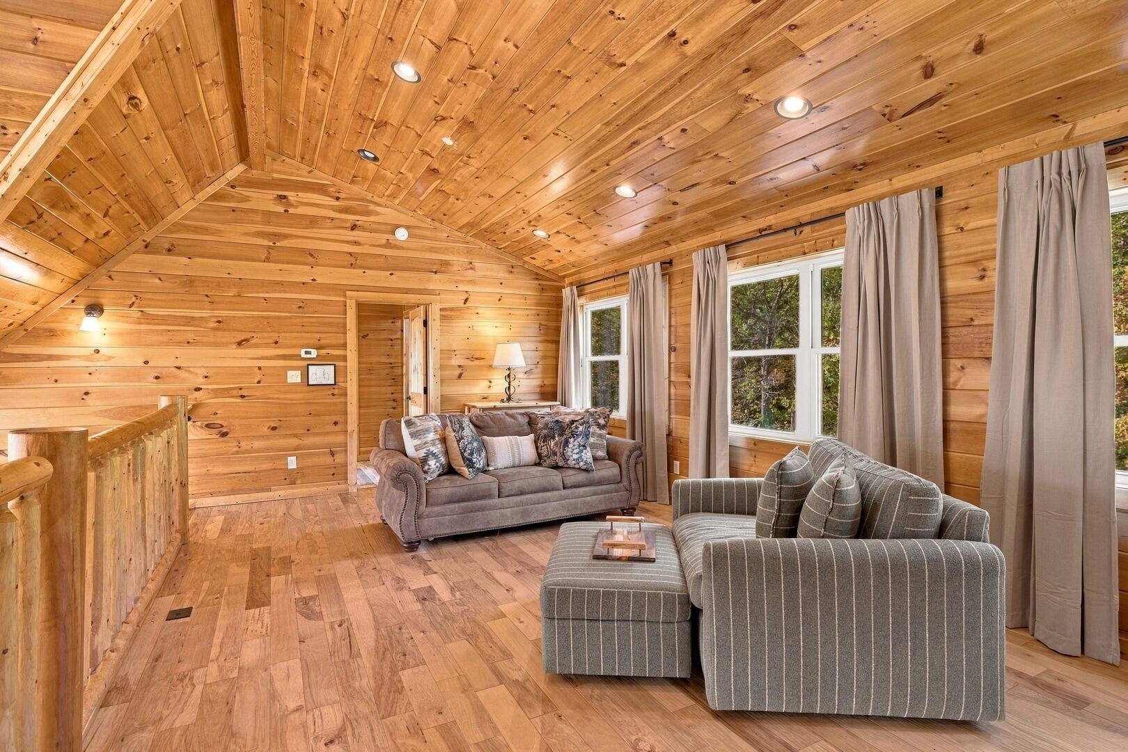A log cabin interior with a wooden ceiling, two sofas, a table, and large windows.