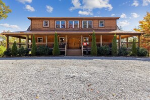 A two-story wooden house with a porch, multiple windows, and a gravel driveway.