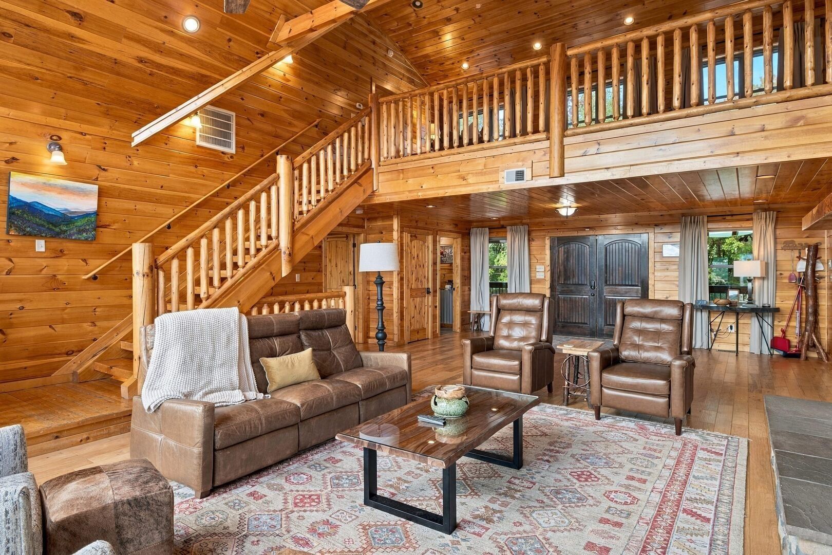 A spacious wooden interior with a staircase, leather furniture, and a view of the outdoors.
