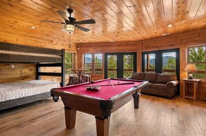 A wooden cabin with a pool table, a sofa, and a bed.