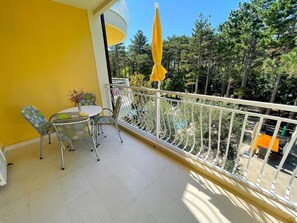 Enjoy the serene views of lush greenery from this balcony with a small table and comfortable seating.