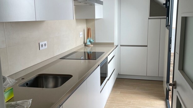 Una cocina moderna con un lavamanos de acero inoxidable, armarios blancos y piso de madera.